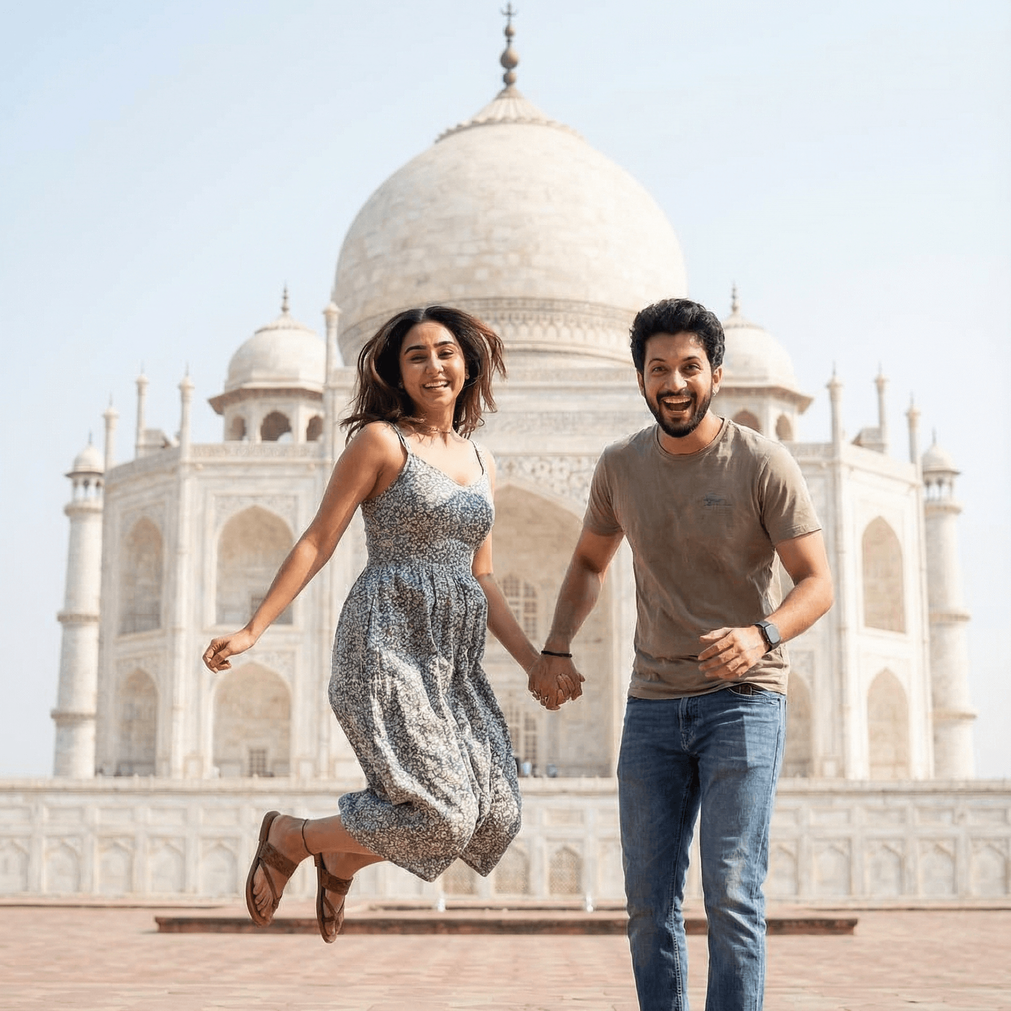 A candid shot of an Indian couple posing playfully in front of an iconic travel landmark (like the Taj Mahal, or a scenic mountain range). The girl is jumping slightly, holding the man's hand, while he grins at the camera. Their expressions are joyful, energetic, and full of wanderlust.